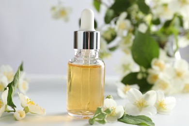 Photo of Essential oil and beautiful jasmine flowers on white table, closeup