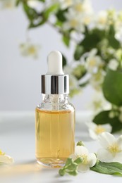 Photo of Essential oil and beautiful jasmine flowers on white table, closeup