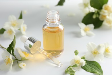 Photo of Essential oil and beautiful jasmine flowers on white table, closeup