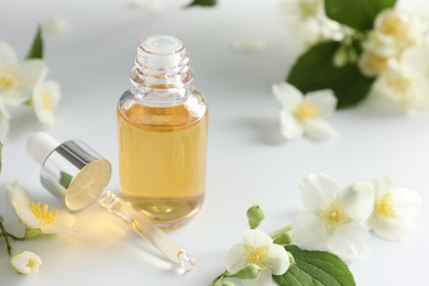 Photo of Essential oil and beautiful jasmine flowers on white table, closeup. Space for text