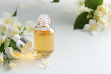 Photo of Essential oil and beautiful jasmine flowers on white table, closeup. Space for text