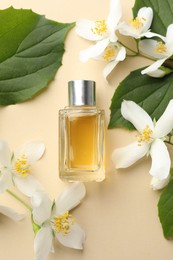 Photo of Bottle of perfume, beautiful jasmine flowers and green leaves on beige background, flat lay