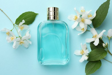 Photo of Bottle of perfume, beautiful jasmine flowers and green leaves on light blue background, flat lay