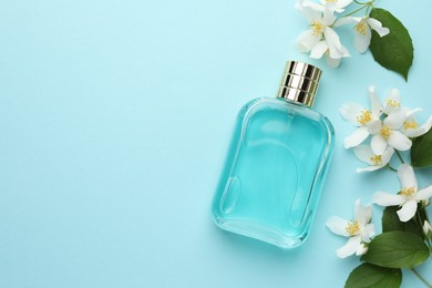 Photo of Bottle of perfume, beautiful jasmine flowers and green leaves on light blue background, flat lay. Space for text