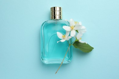 Photo of Bottle of perfume, beautiful jasmine flowers and green leaf on light blue background, top view