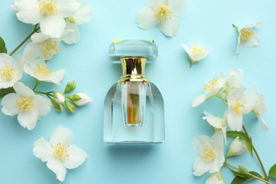 Photo of Bottle of perfume and beautiful jasmine flowers on light blue background, flat lay