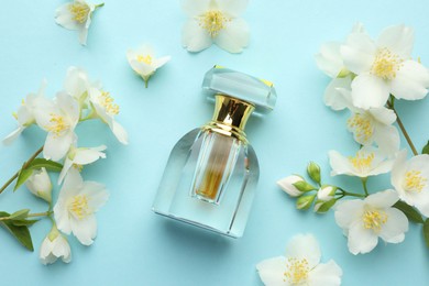 Photo of Bottle of perfume and beautiful jasmine flowers on light blue background, flat lay