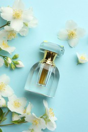Photo of Bottle of perfume and beautiful jasmine flowers on light blue background, flat lay