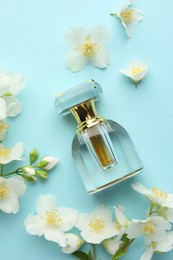 Photo of Bottle of perfume and beautiful jasmine flowers on light blue background, flat lay