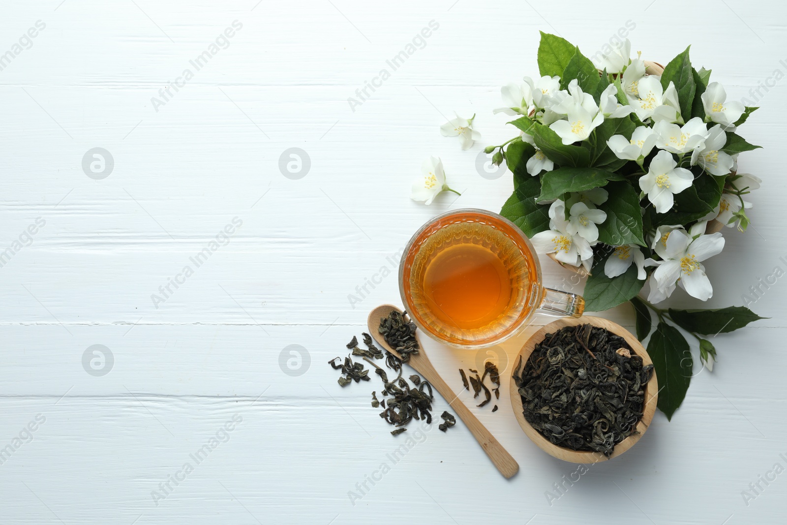 Aromatic jasmine tea in glass cup, flowers and leaves on white wooden table, flat lay. Space for text Photo of Aromatic jasmine tea in glass cup, flowers and leaves on white wooden table, flat lay. Space for text