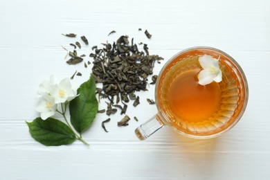 Photo of Aromatic jasmine tea in glass cup, flowers and leaves on white wooden table, flat lay