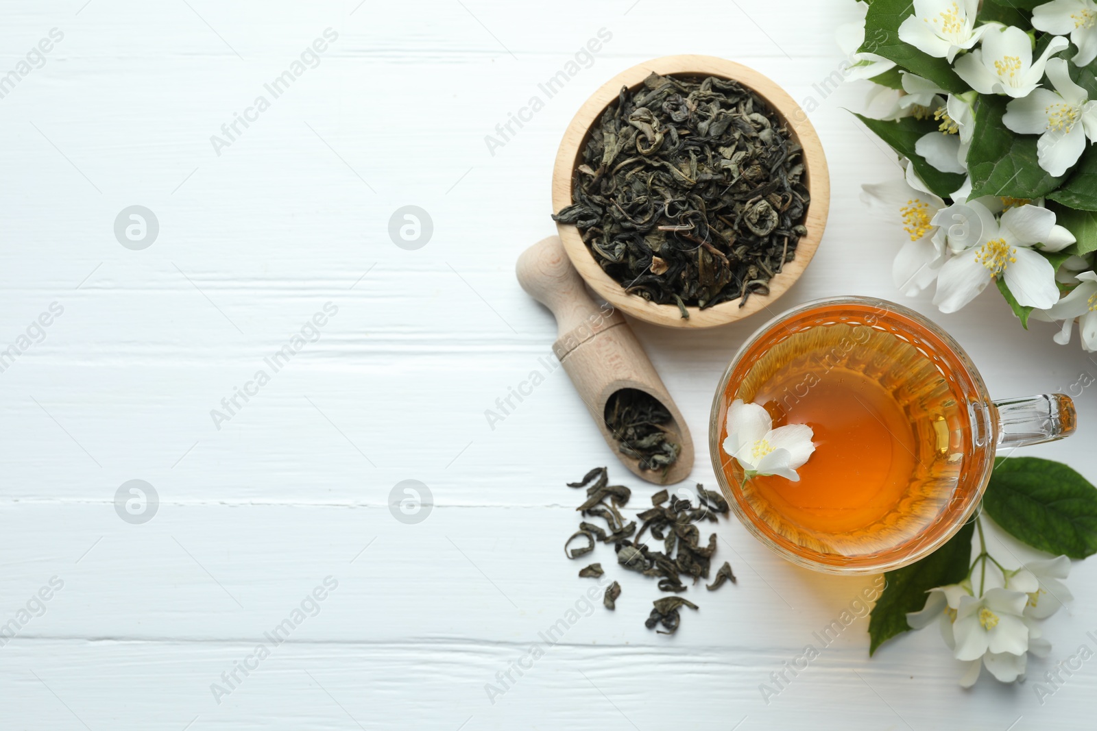 Aromatic jasmine tea in glass cup, flowers and leaves on white wooden table, flat lay. Space for text Photo of Aromatic jasmine tea in glass cup, flowers and leaves on white wooden table, flat lay. Space for text