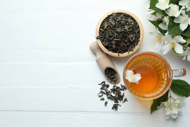 Photo of Aromatic jasmine tea in glass cup, flowers and leaves on white wooden table, flat lay. Space for text