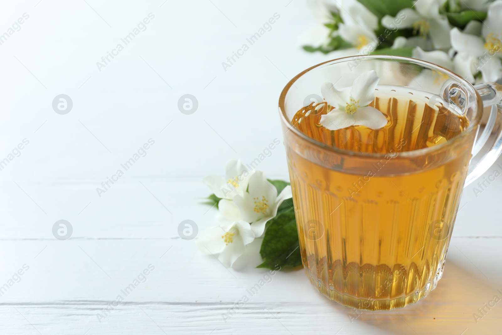 Aromatic jasmine tea in glass cup, flowers and green leaves on white wooden table, closeup. Space for text Photo of Aromatic jasmine tea in glass cup, flowers and green leaves on white wooden table, closeup. Space for text