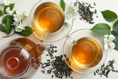 Photo of Aromatic jasmine tea in glass cups, flowers and leaves on white table, flat lay