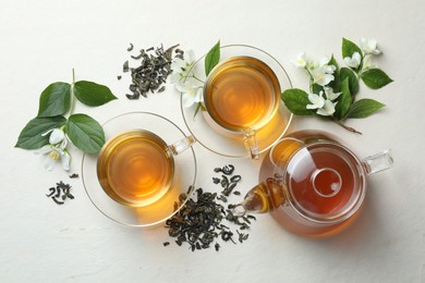 Photo of Aromatic jasmine tea in glass cups, flowers and leaves on white table, flat lay