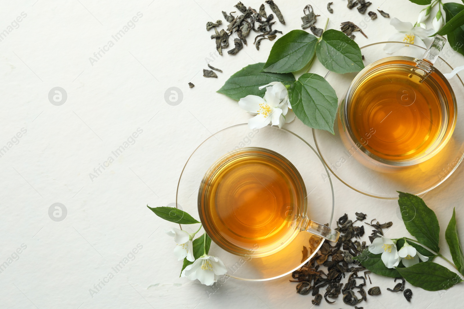 Aromatic jasmine tea in glass cups, flowers and leaves on white table, flat lay. Space for text Photo of Aromatic jasmine tea in glass cups, flowers and leaves on white table, flat lay. Space for text