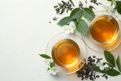 Photo of Aromatic jasmine tea in glass cups, flowers and leaves on white table, flat lay. Space for text