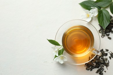 Photo of Aromatic jasmine tea in glass cup, flowers and leaves on white table, flat lay. Space for text