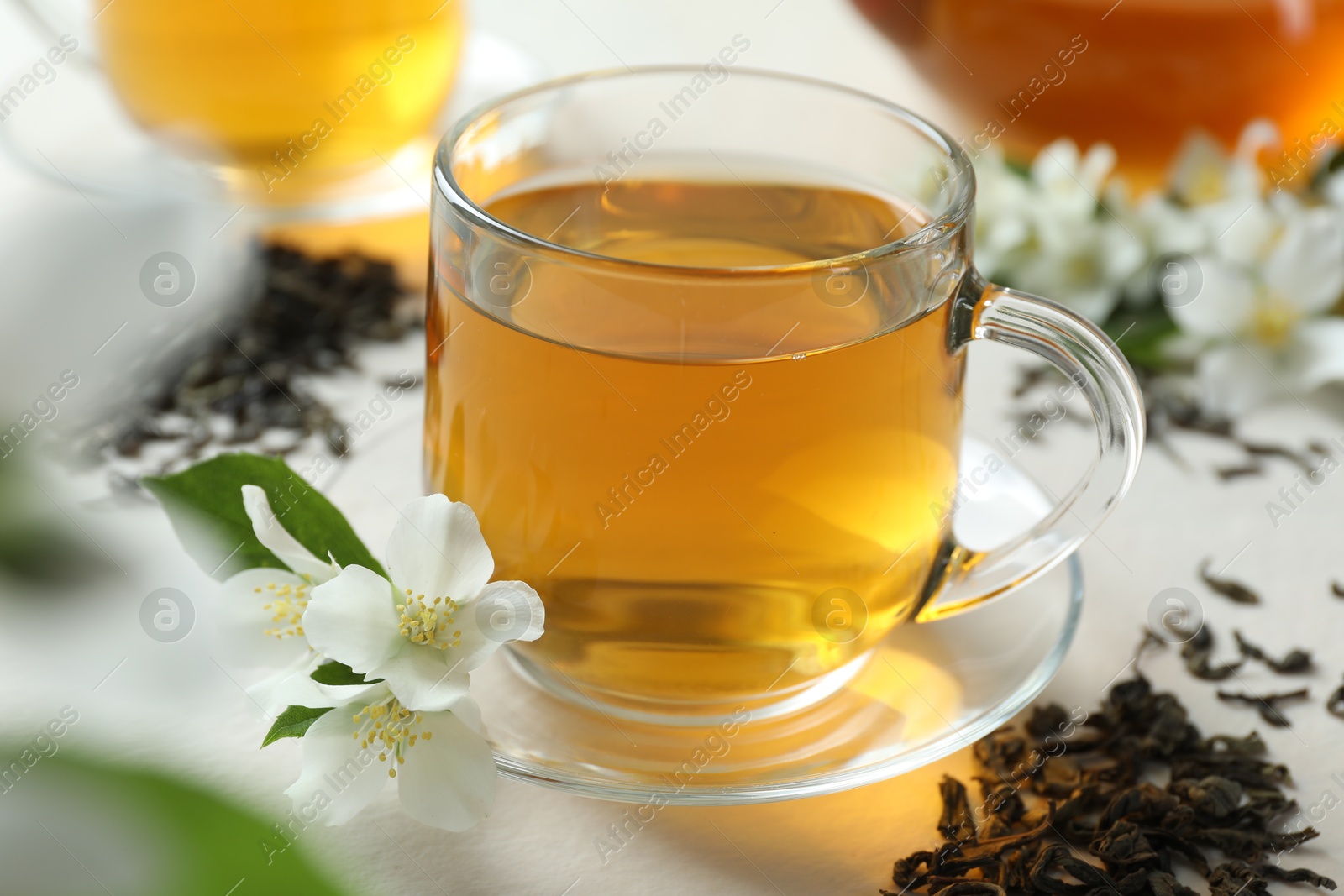 Aromatic jasmine tea in glass cup, flowers and dried leaves on white table, closeup Photo of Aromatic jasmine tea in glass cup, flowers and dried leaves on white table, closeup