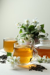 Photo of Aromatic jasmine tea in glass cups, teapot, flowers and dried leaves on white table