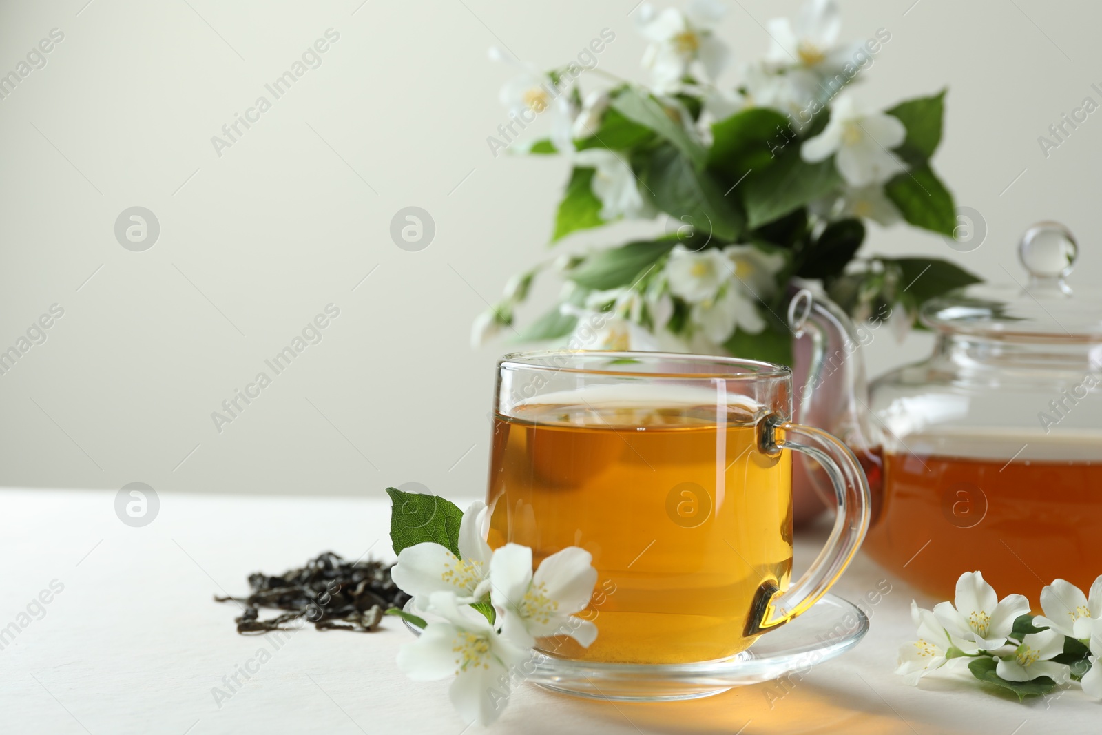 Aromatic jasmine tea in glass cup, teapot, flowers and dried leaves on white table, closeup. Space for text Photo of Aromatic jasmine tea in glass cup, teapot, flowers and dried leaves on white table, closeup. Space for text