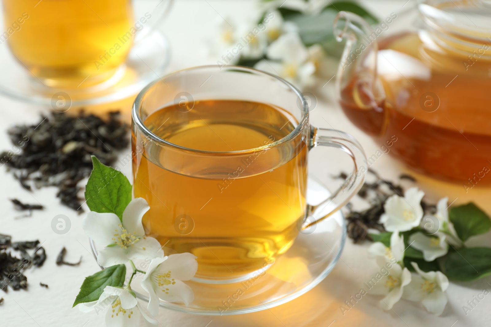 Aromatic jasmine tea in glass cup, teapot, flowers and dried leaves on white table, closeup Photo of Aromatic jasmine tea in glass cup, teapot, flowers and dried leaves on white table, closeup