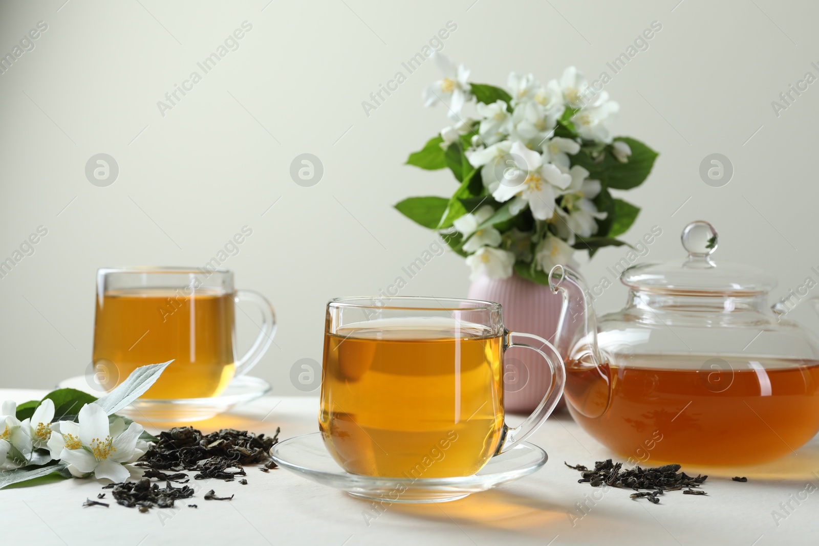 Aromatic jasmine tea in glass cups, teapot, flowers and dried leaves on white table Photo of Aromatic jasmine tea in glass cups, teapot, flowers and dried leaves on white table