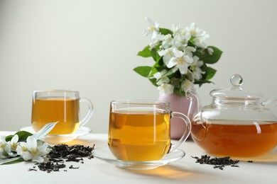 Photo of Aromatic jasmine tea in glass cups, teapot, flowers and dried leaves on white table