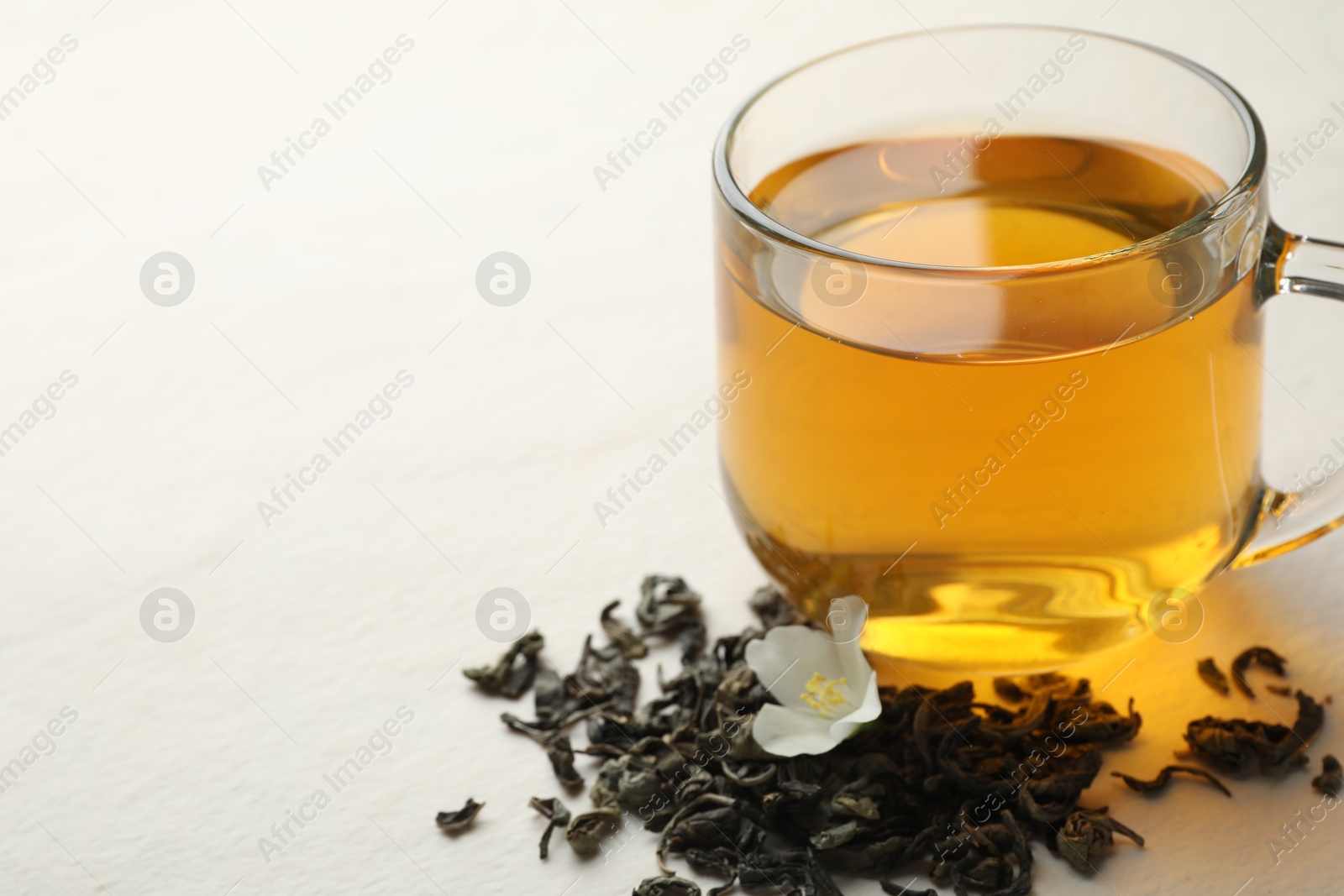Aromatic jasmine tea in glass cup, flower and dried leaves on white table, closeup. Space for text Photo of Aromatic jasmine tea in glass cup, flower and dried leaves on white table, closeup. Space for text