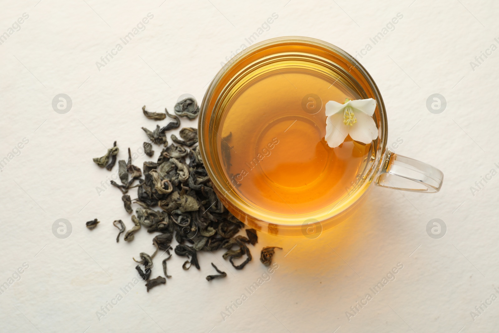 Aromatic jasmine tea in glass cup, flower and dried leaves on white table, flat lay Photo of Aromatic jasmine tea in glass cup, flower and dried leaves on white table, flat lay