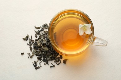 Photo of Aromatic jasmine tea in glass cup, flower and dried leaves on white table, flat lay