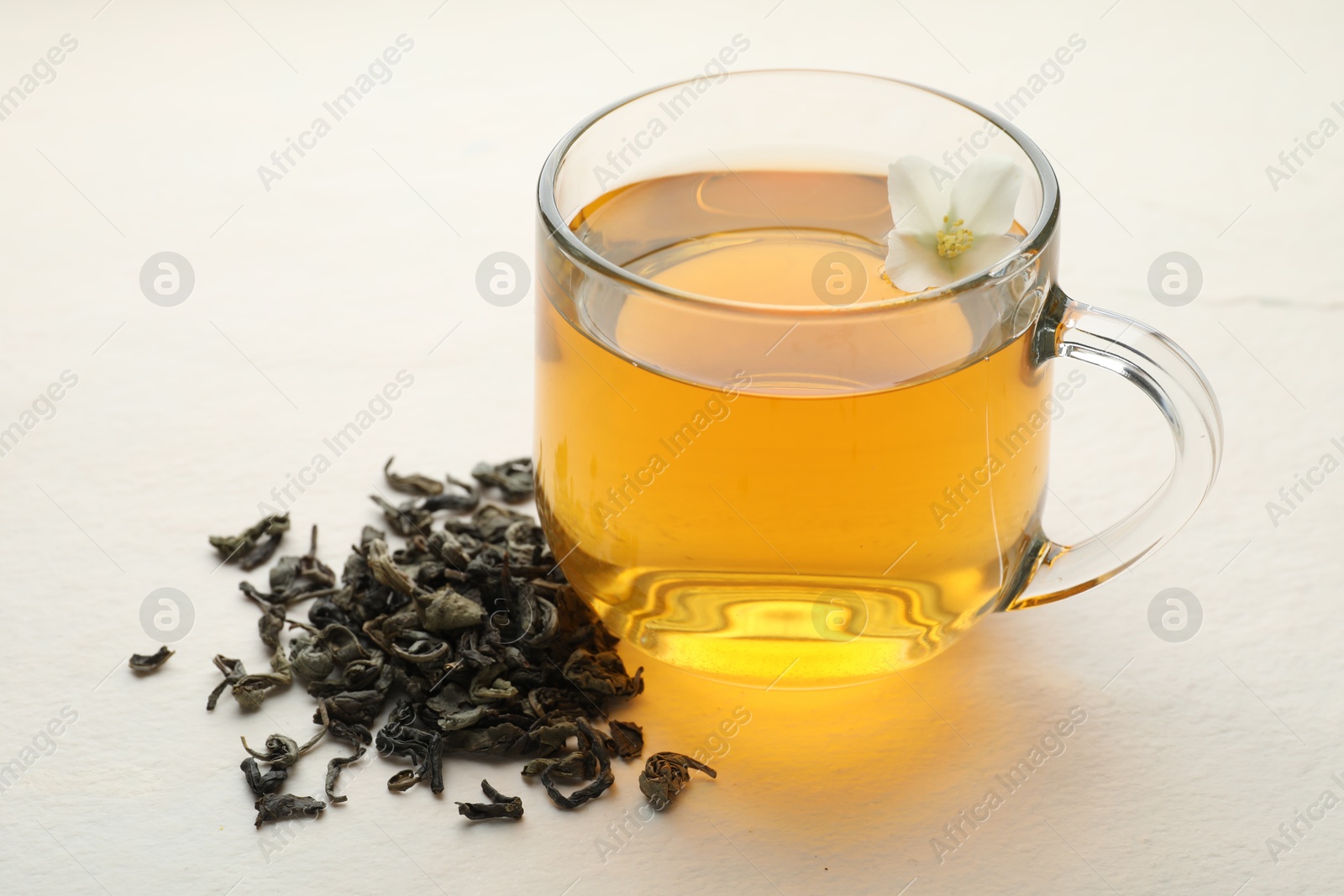 Aromatic jasmine tea in glass cup, flower and dried leaves on white table, closeup Photo of Aromatic jasmine tea in glass cup, flower and dried leaves on white table, closeup