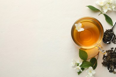 Photo of Aromatic jasmine tea in glass cup, flowers and leaves on white table, flat lay. Space for text
