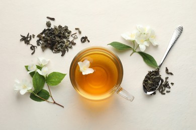Photo of Aromatic jasmine tea in glass cup, flowers and leaves on white table, flat lay
