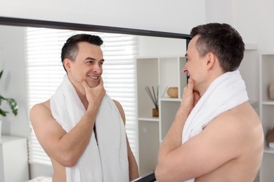 Photo of Smiling man after shaving looking at mirror in bathroom