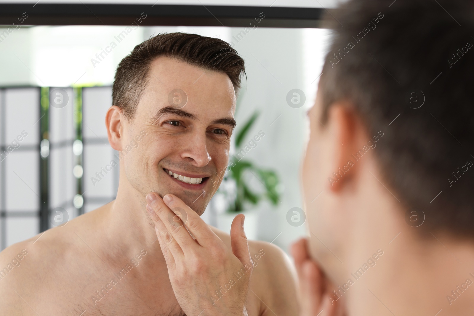 Smiling man after shaving looking at mirror in bathroom Photo of Smiling man after shaving looking at mirror in bathroom