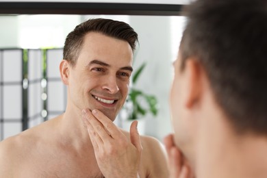 Photo of Smiling man after shaving looking at mirror in bathroom