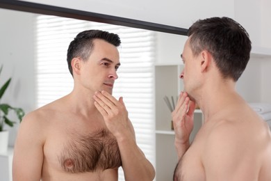 Photo of Handsome man after shaving looking at mirror in bathroom