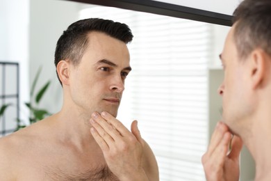 Photo of Handsome man after shaving looking at mirror in bathroom