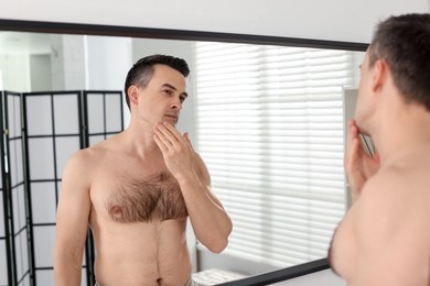 Photo of Handsome man after shaving looking at mirror in bathroom