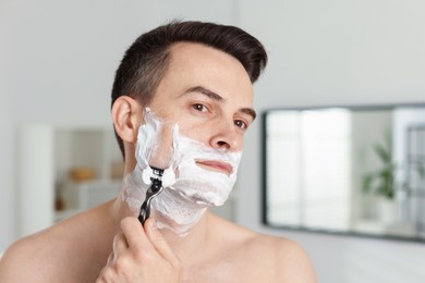 Photo of Handsome man shaving with razor at home