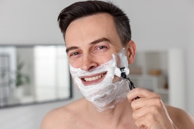Photo of Smiling man shaving with razor at home