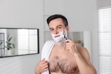 Photo of Handsome man shaving with razor at home