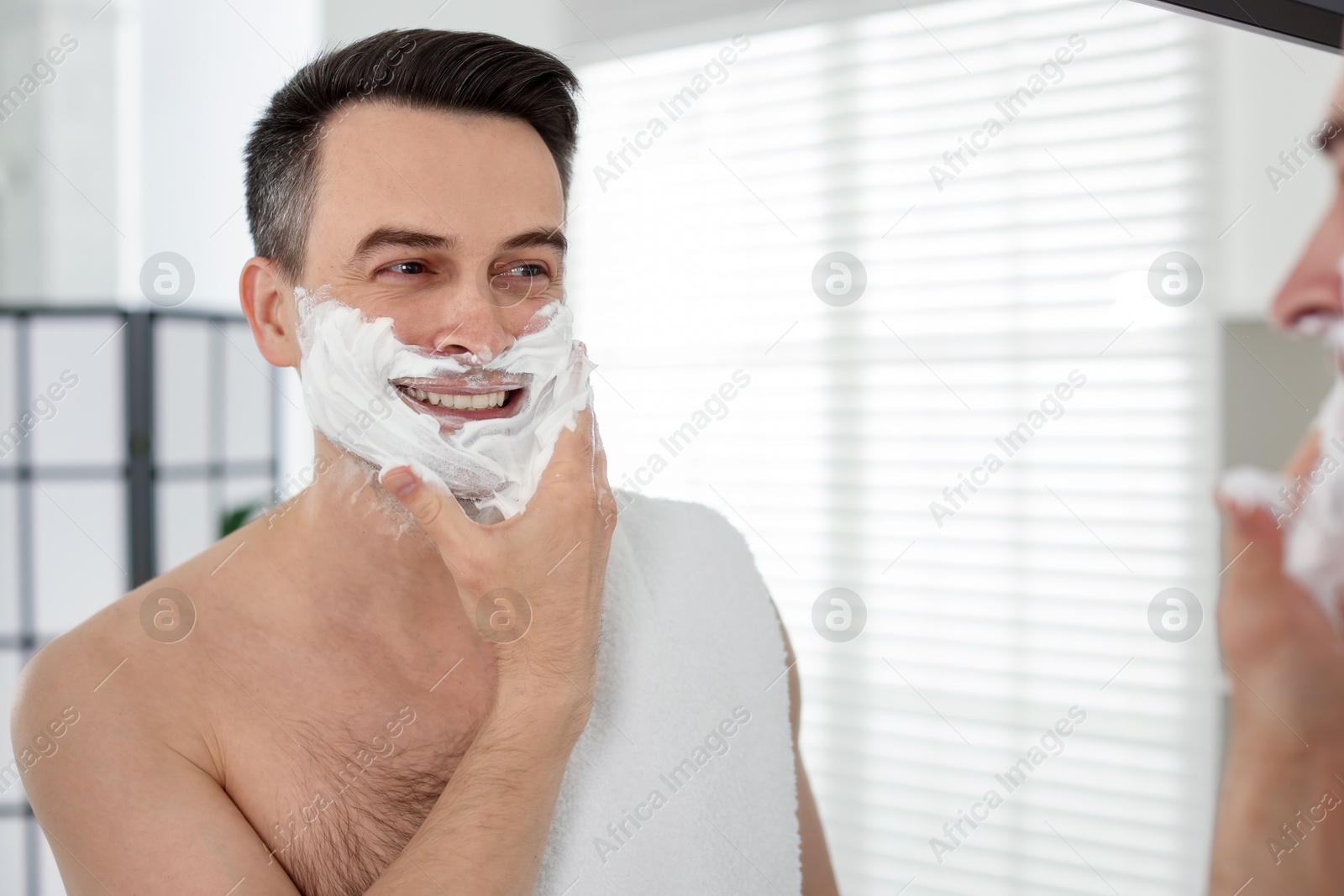 Smiling man applying shaving foam near mirror in bathroom Photo of Smiling man applying shaving foam near mirror in bathroom