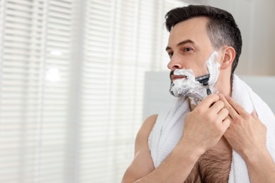 Photo of Handsome man shaving with razor at home. Space for text