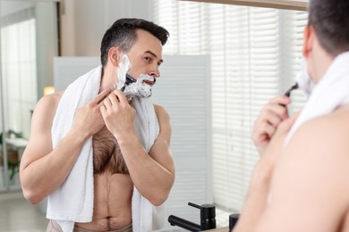 Photo of Handsome man shaving with razor near mirror at home