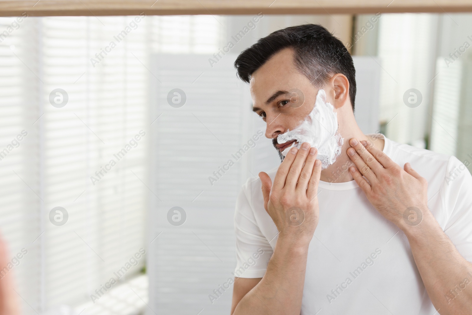 Handsome man applying shaving foam near mirror in bathroom. Space for text Photo of Handsome man applying shaving foam near mirror in bathroom. Space for text