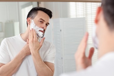 Photo of Handsome man applying shaving foam near mirror in bathroom
