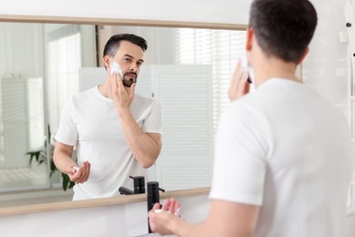 Photo of Handsome man applying shaving foam near mirror in bathroom